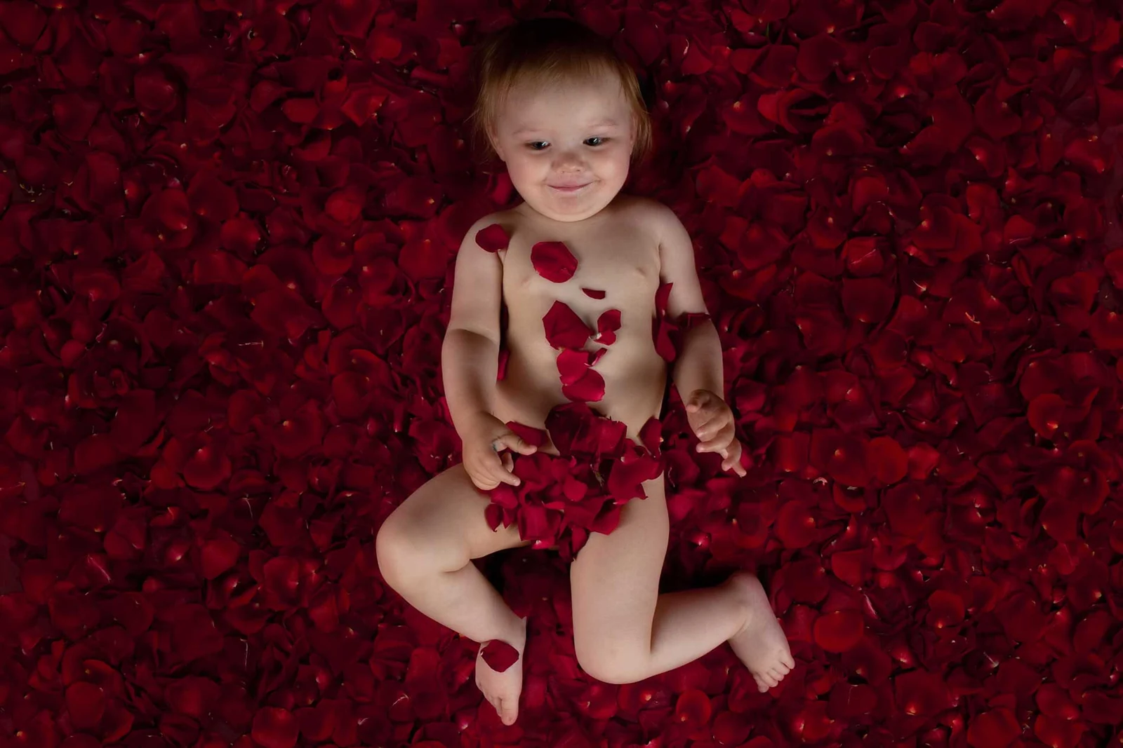 Baby zwischen roten Rosenblättern im Fotostudio
