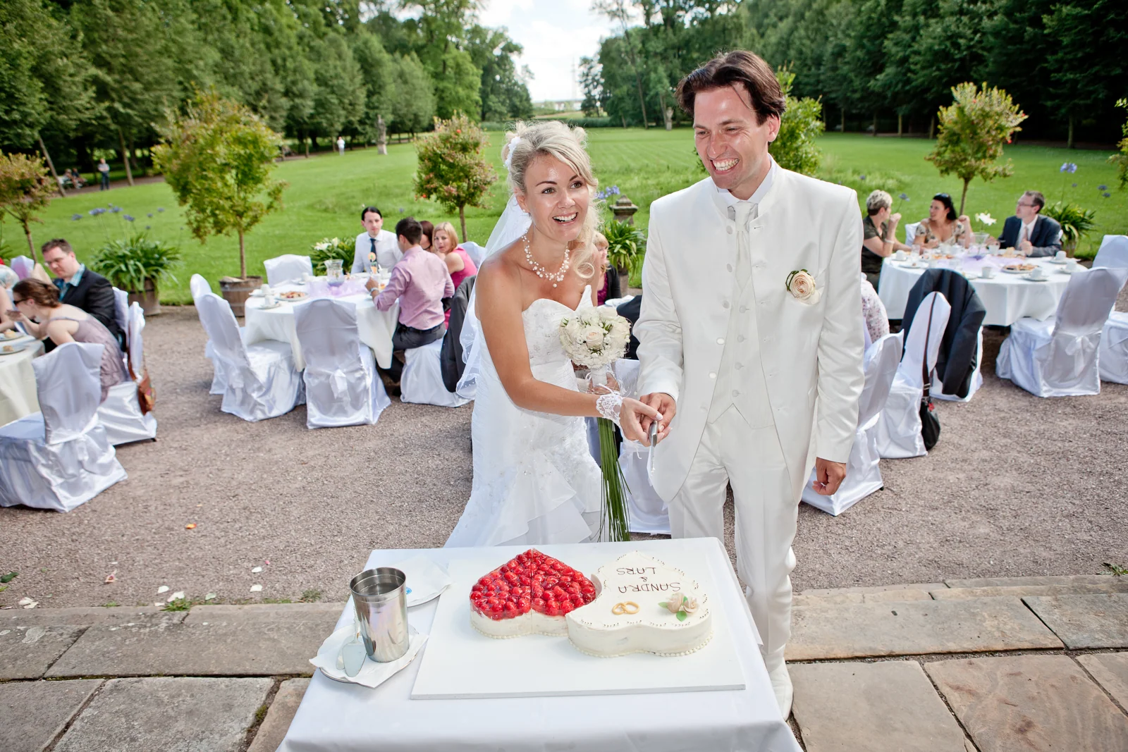 Das Brautpaar bei der Hochzeitstorte im Schlossgarten – Hochzeitsreportage von Sandra und Lars