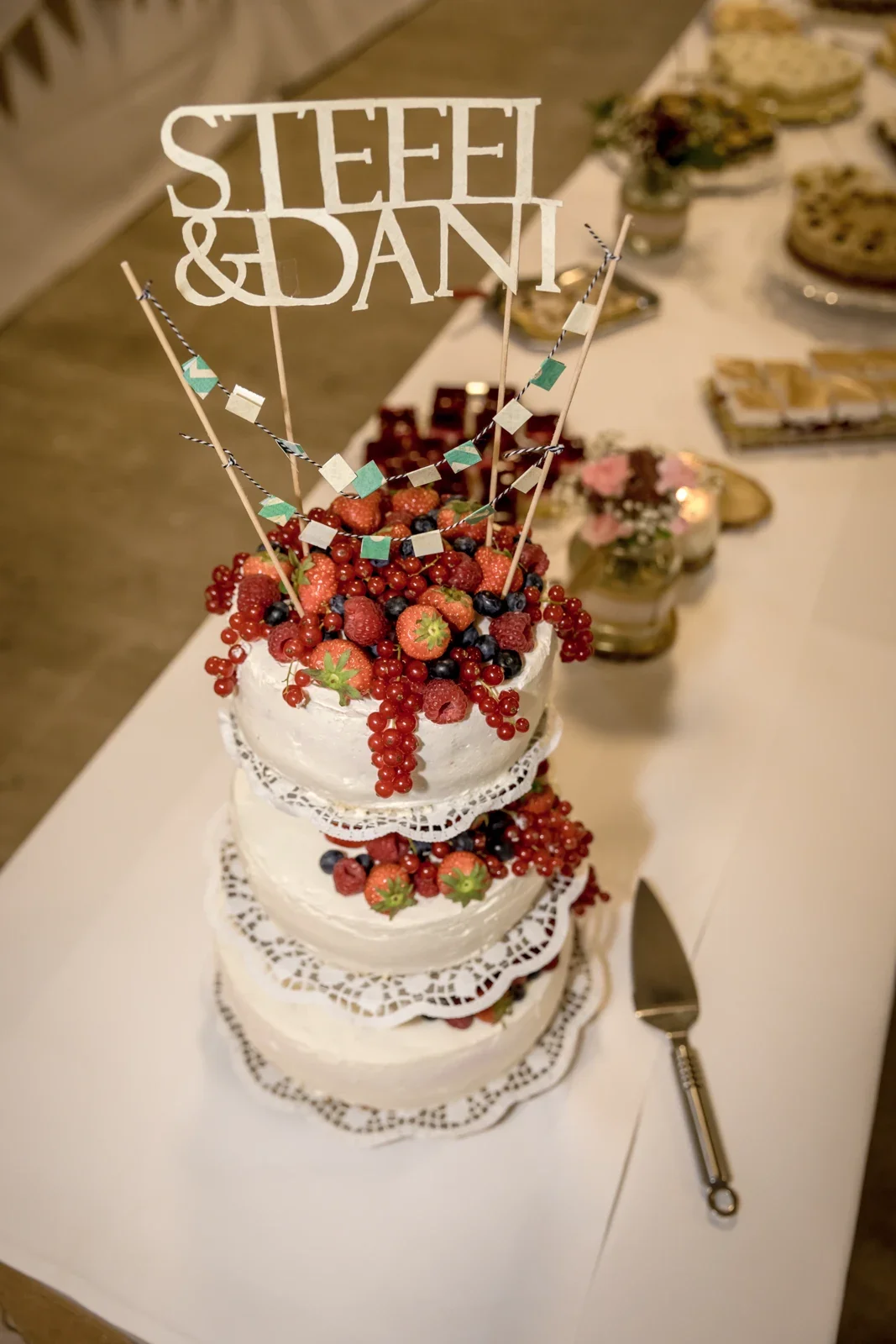 Die Hochzeitstorte mit Beeren und dem Namen des Brautpaars – Hochzeit von Daniel und Steffi auf Schloss Heringen