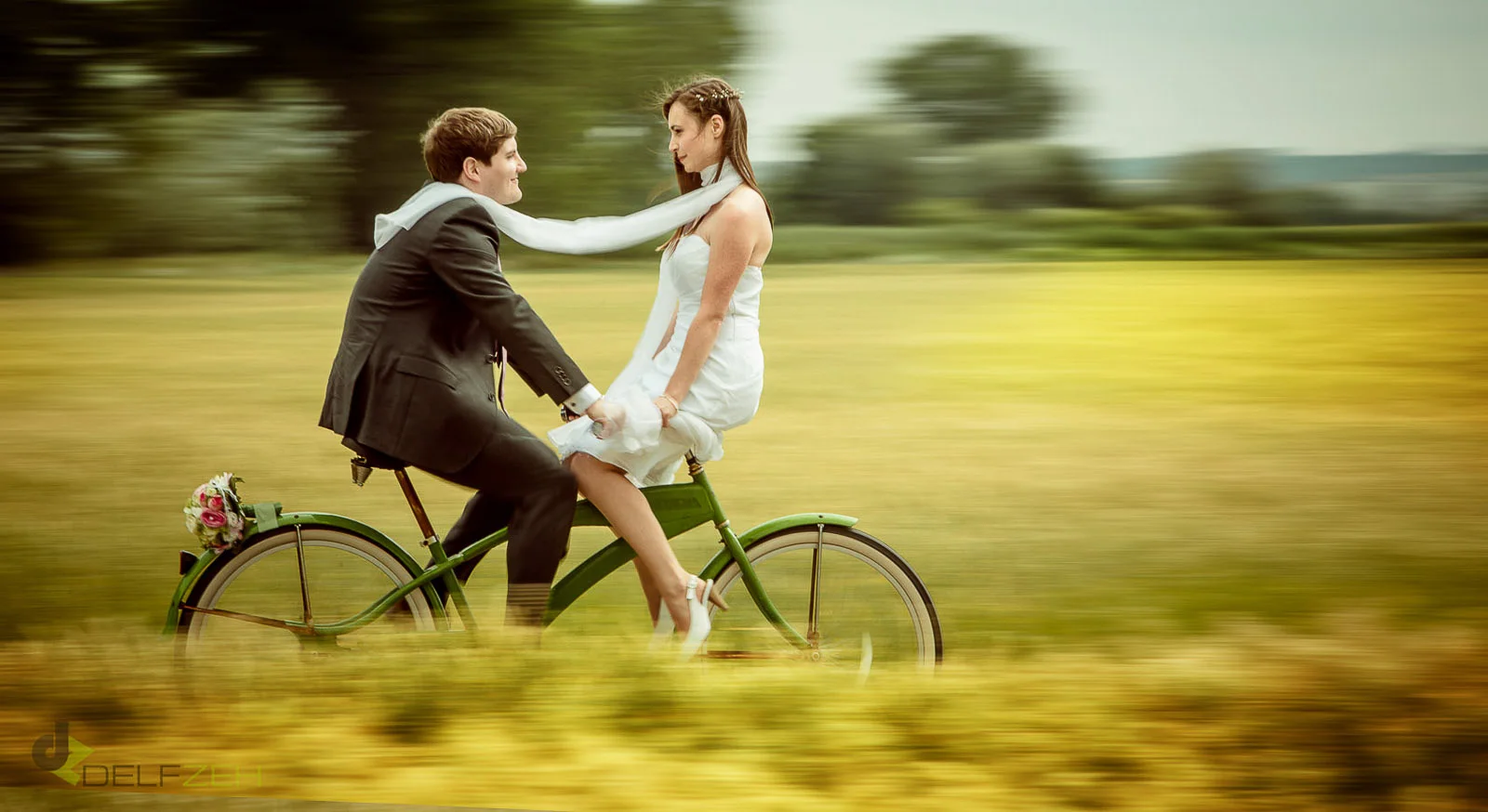 Brautpaar fährt gemeinsam mit dem Fahrrad über eine Wiese Brautpaar fährt gemeinsam mit dem Fahrrad über eine Wiese