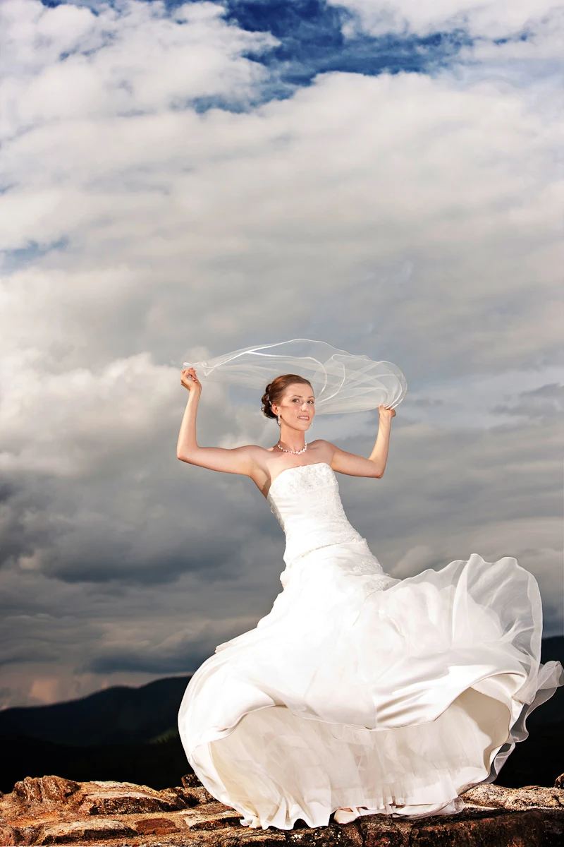 Braut im wehenden Kleid vor dramatischen Wolken