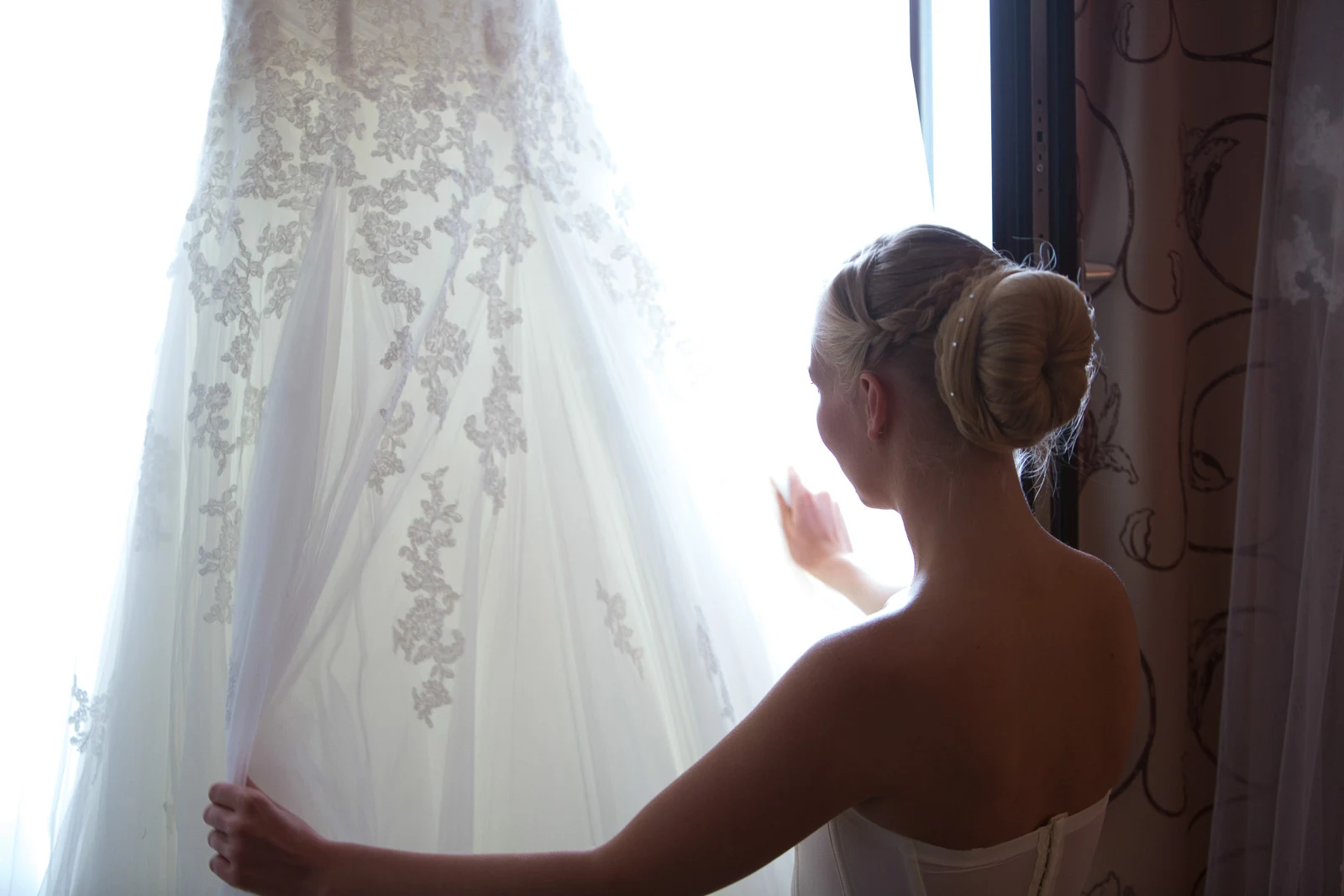 Braut am Fenster neben ihrem Brautkleid