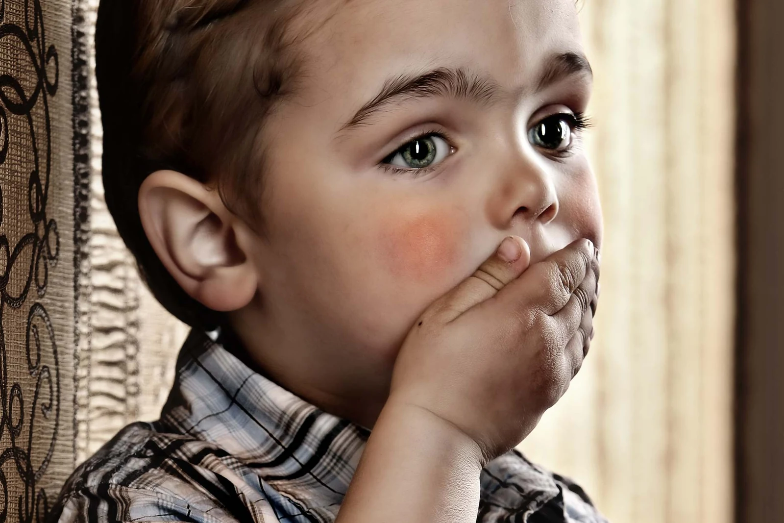 Kinderportrait am Fenster mit den Händen vor dem Mund