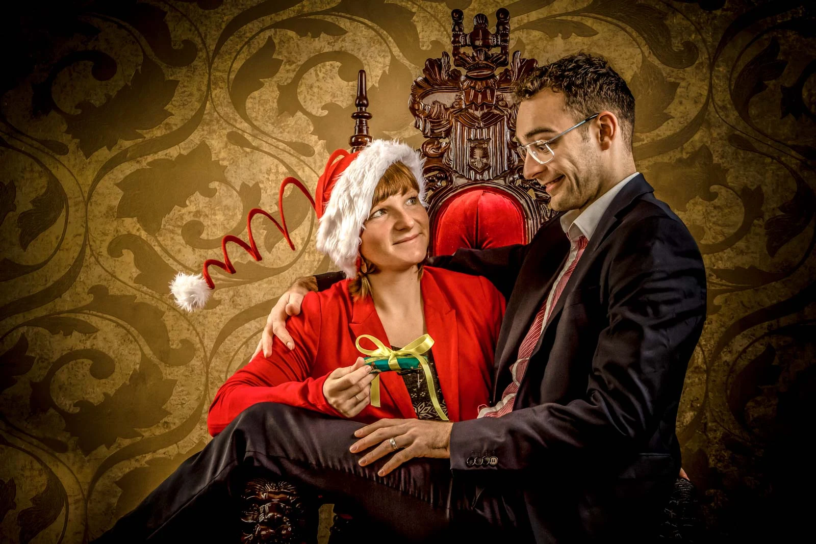 Paarportrait mit Weihnachtsmütze und Geschenk auf einem verzierten Sessel