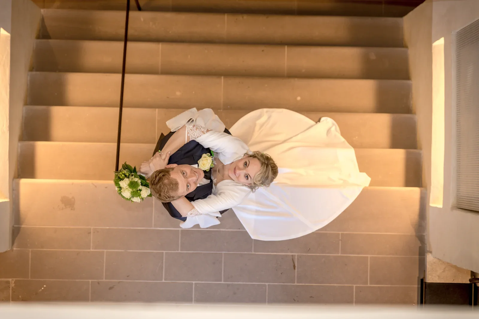 Ein Blick von oben auf das Brautpaar im Treppenhaus – Winterhochzeit von Anika und Marcus auf Schloss Ettersburg und in Weimar